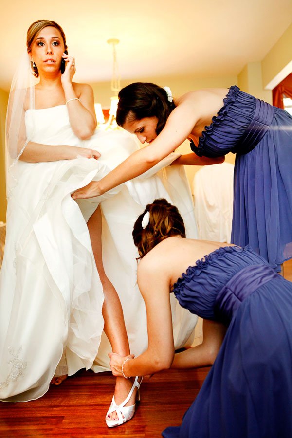 Bride on Cell Phone in Wedding Dress getting garter belt put on by bridesmaids, Allie and Matt